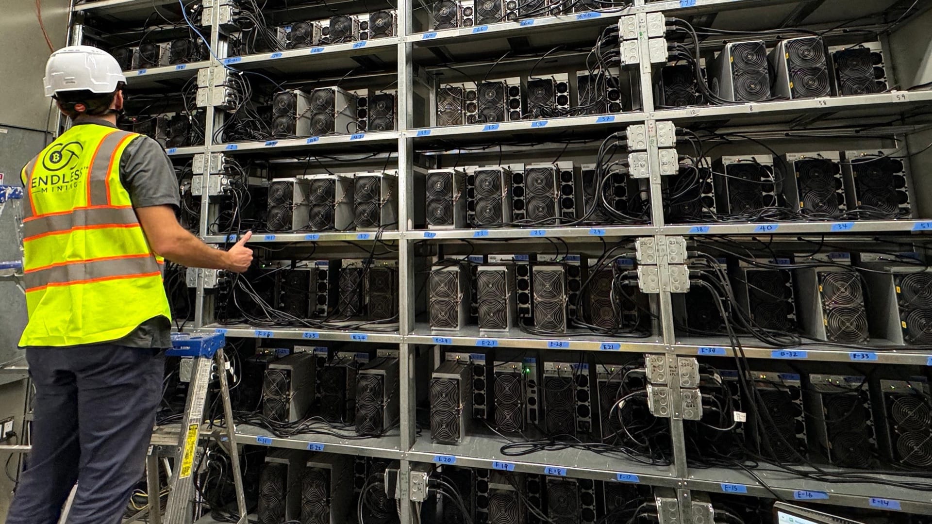 An Endless Mining technician in a hi-vis vest checking racks of hosted ASIC miners